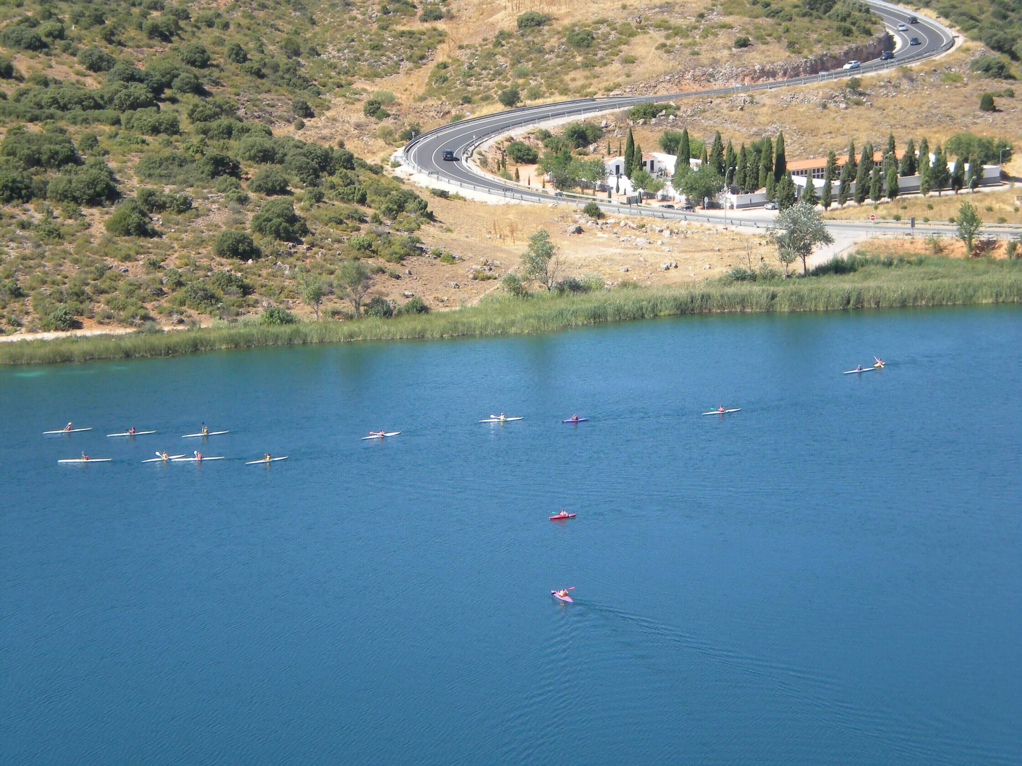 A lake with several boats, a winding road, and a hilly landscape with sparse vegetation.