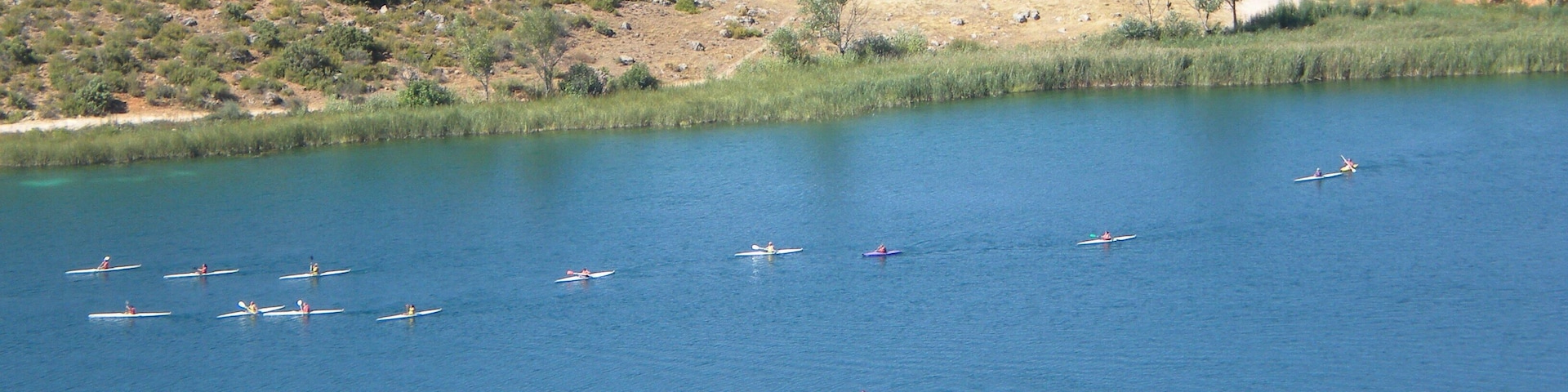 A lake with several boats, a winding road, and a hilly landscape with sparse vegetation.