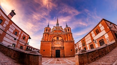 Uma igreja histórica com uma cúpula central e duas torres sineiras, rodeada por ruas de calçada e edifícios vizinhos.