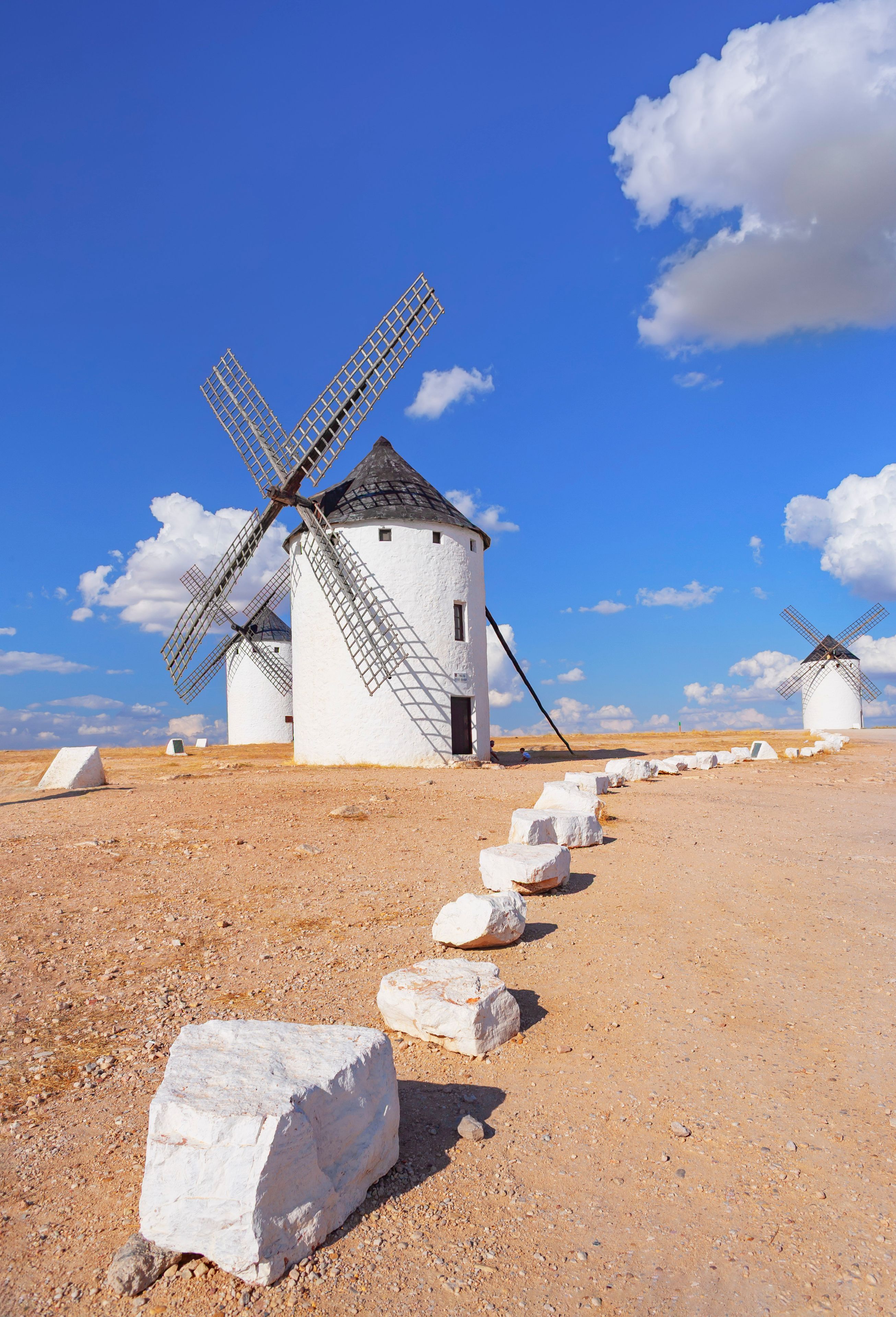 Una hilera de molinos de viento tradicionales en un paisaje árido y abierto, bajo un cielo azul despejado.