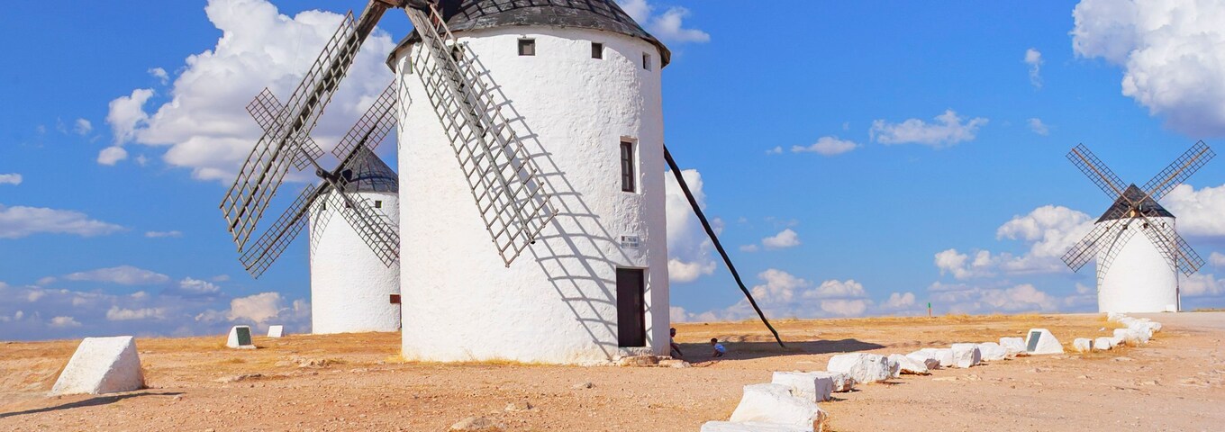 Una hilera de molinos de viento tradicionales en un paisaje árido y abierto, bajo un cielo azul despejado.