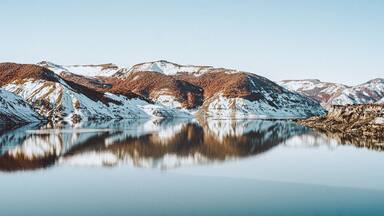 Paisaje montañoso con picos nevados y un lago tranquilo que refleja el entorno.