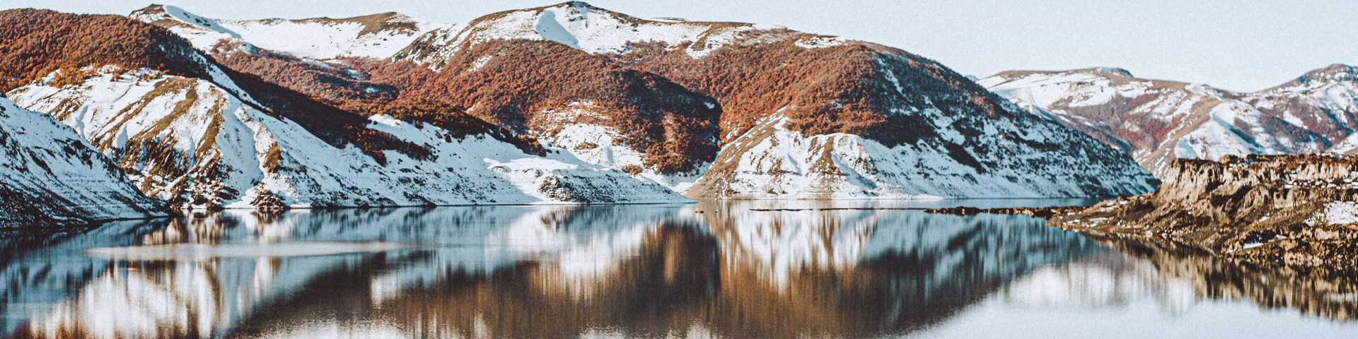 Paisaje montañoso con picos nevados y un lago tranquilo que refleja el entorno.