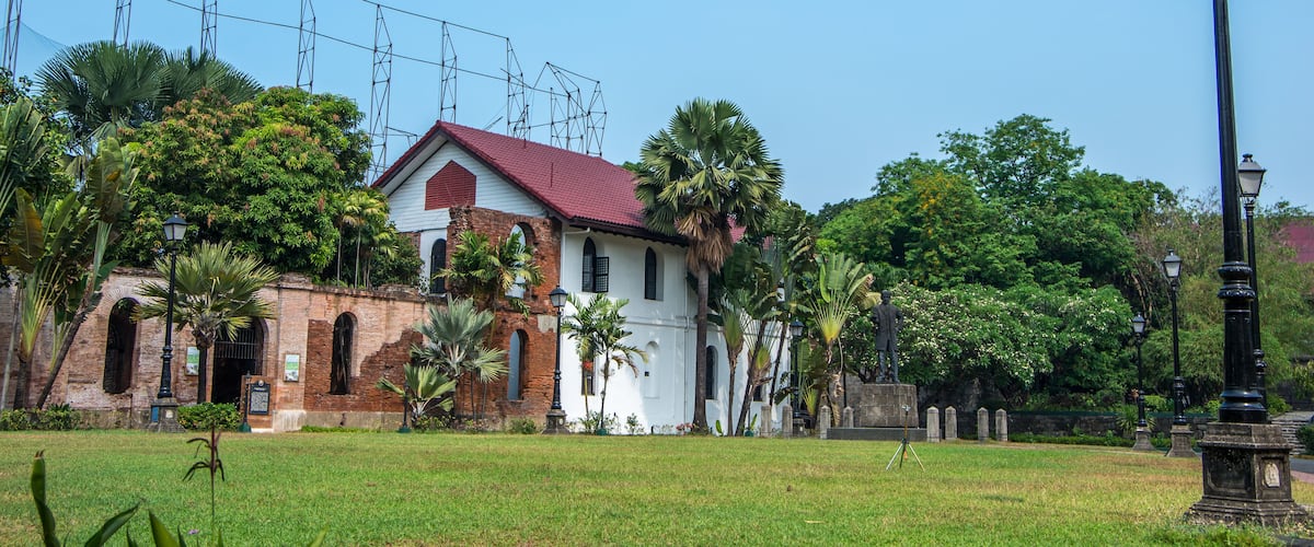 A historic building with a red roof, surrounded by lush greenery and palm trees.