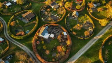 An aerial view of a residential area with houses arranged in circular patterns, surrounded by well-maintained gardens and trees.