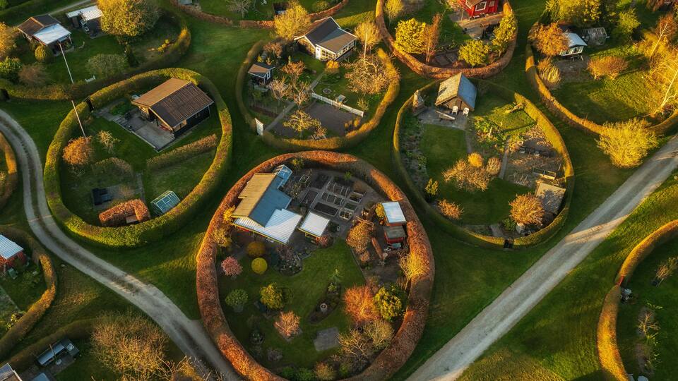 An aerial view of a residential area with houses arranged in circular patterns, surrounded by well-maintained gardens and trees.