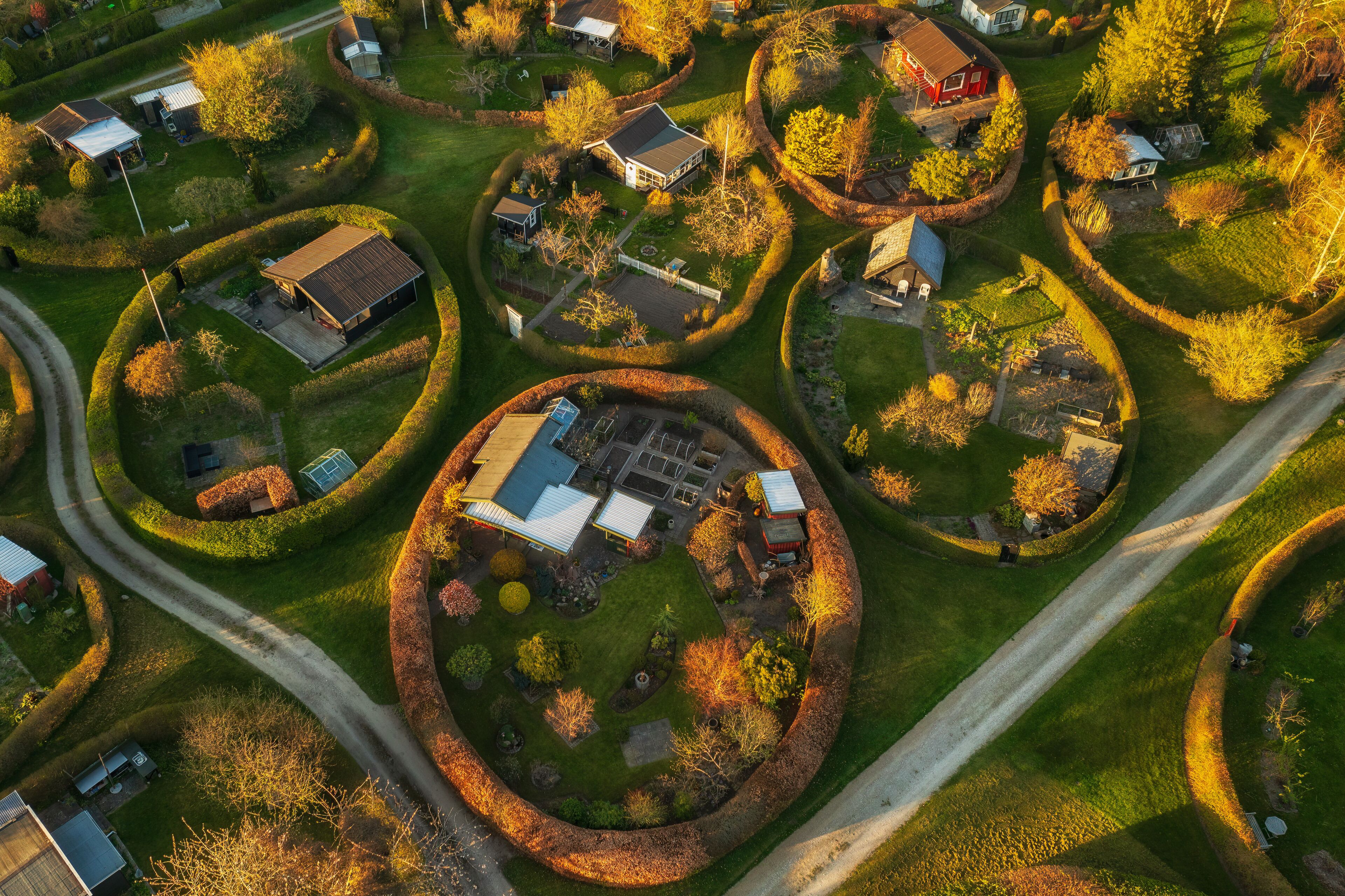 An aerial view of a residential area with houses arranged in circular patterns, surrounded by well-maintained gardens and trees.