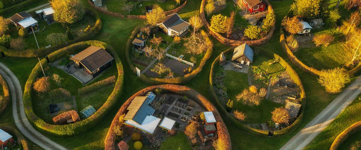 An aerial view of a residential area with houses arranged in circular patterns, surrounded by well-maintained gardens and trees.