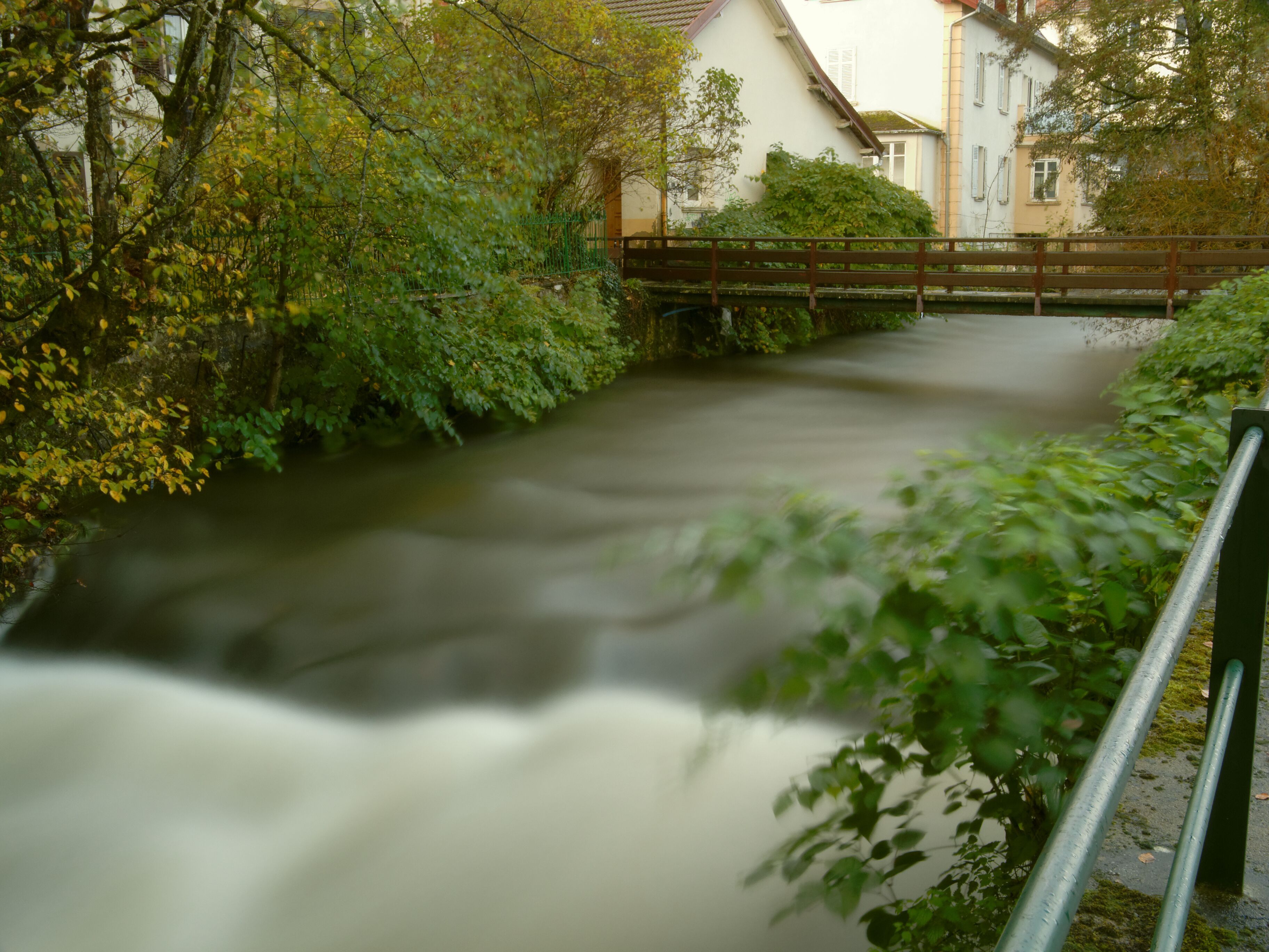 A river flowing through a town with greenery and buildings.