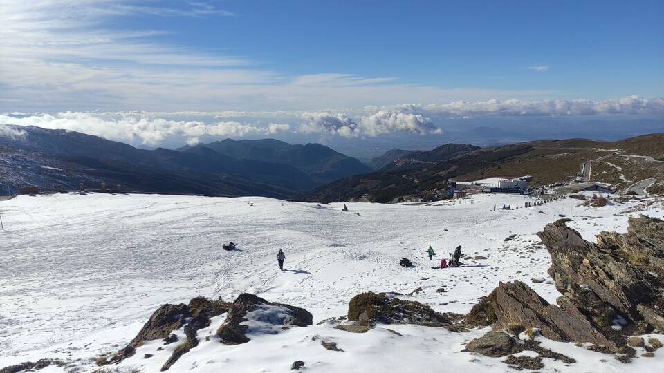 A snowy mountain landscape with rocky outcrops and a clear blue sky.