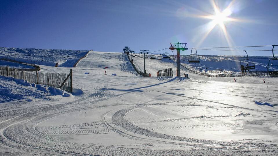 A snowy ski slope with ski lifts, a fence, and a clear sky.