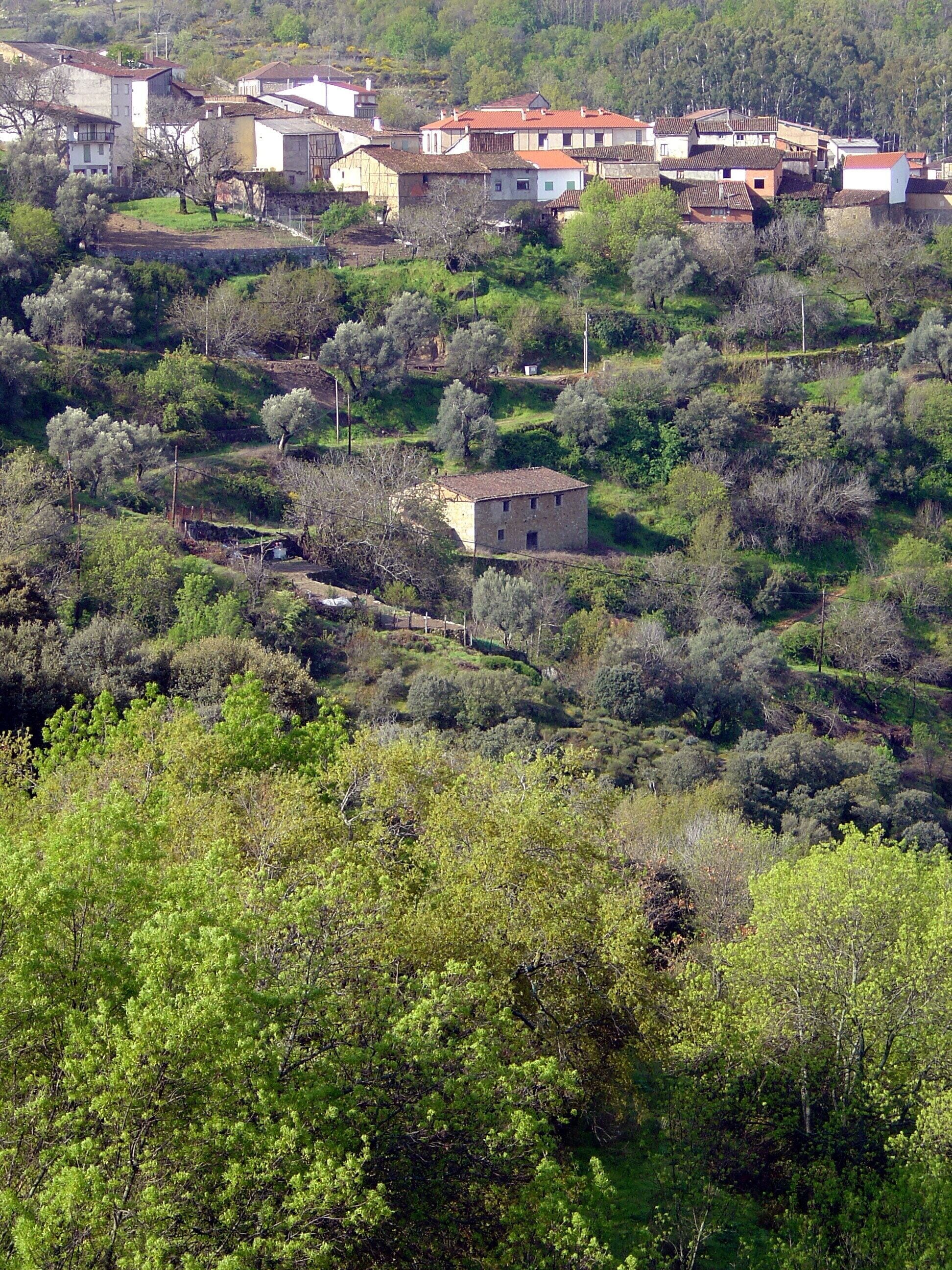 A rural village with stone houses surrounded by lush greenery and hills.