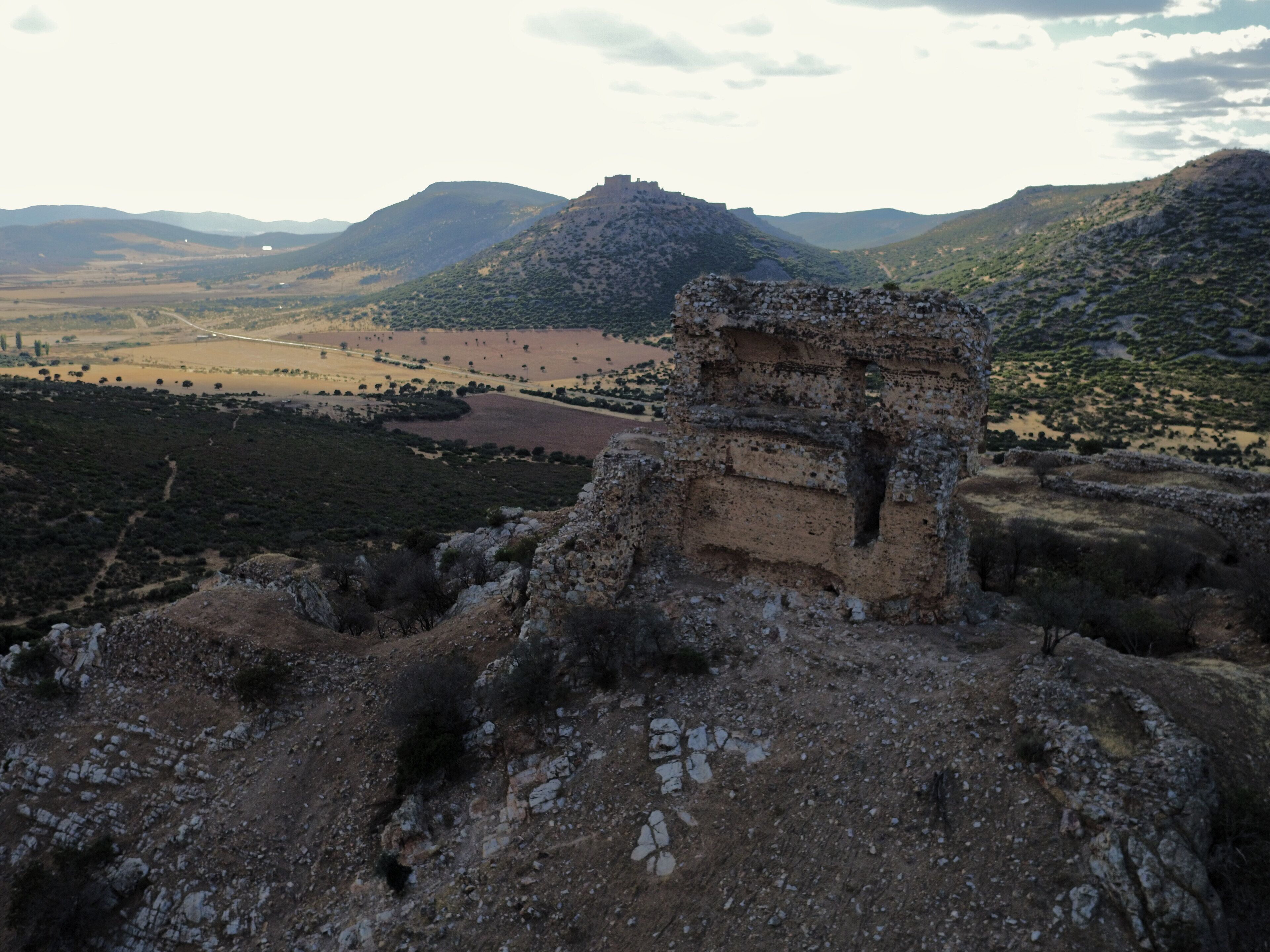 A historical stone structure amidst a mountainous landscape with a river and fields.