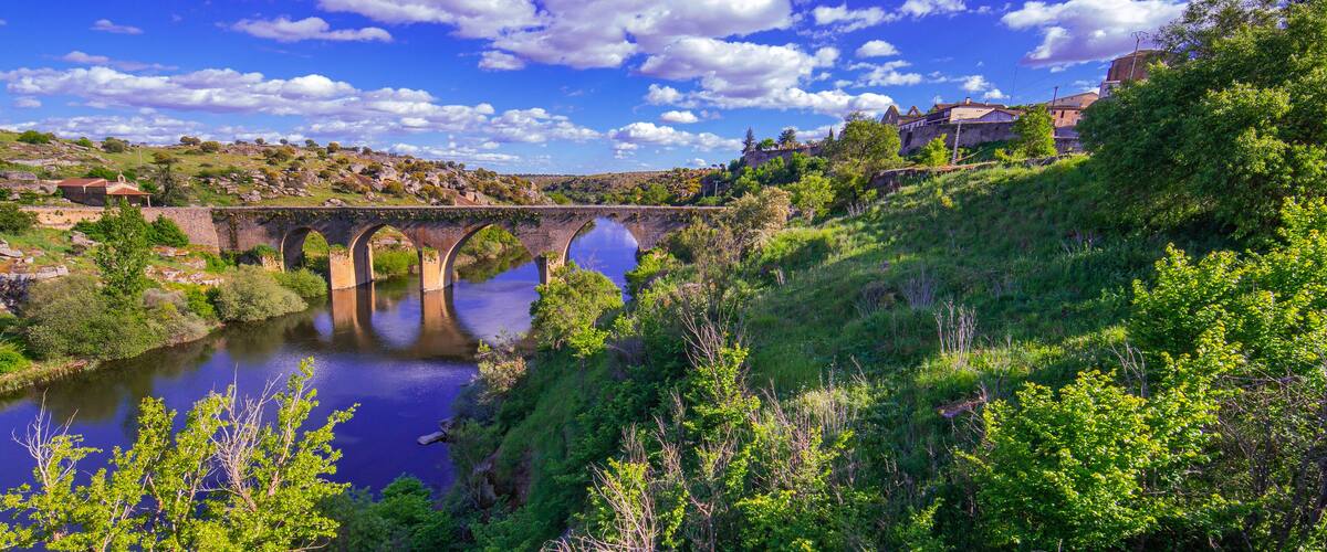 A stone bridge over a river, surrounded by lush greenery and hills.