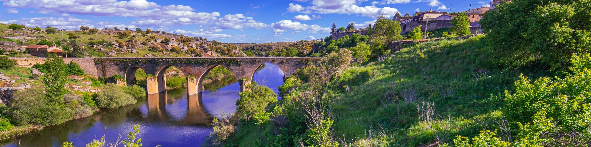 A stone bridge over a river, surrounded by lush greenery and hills.