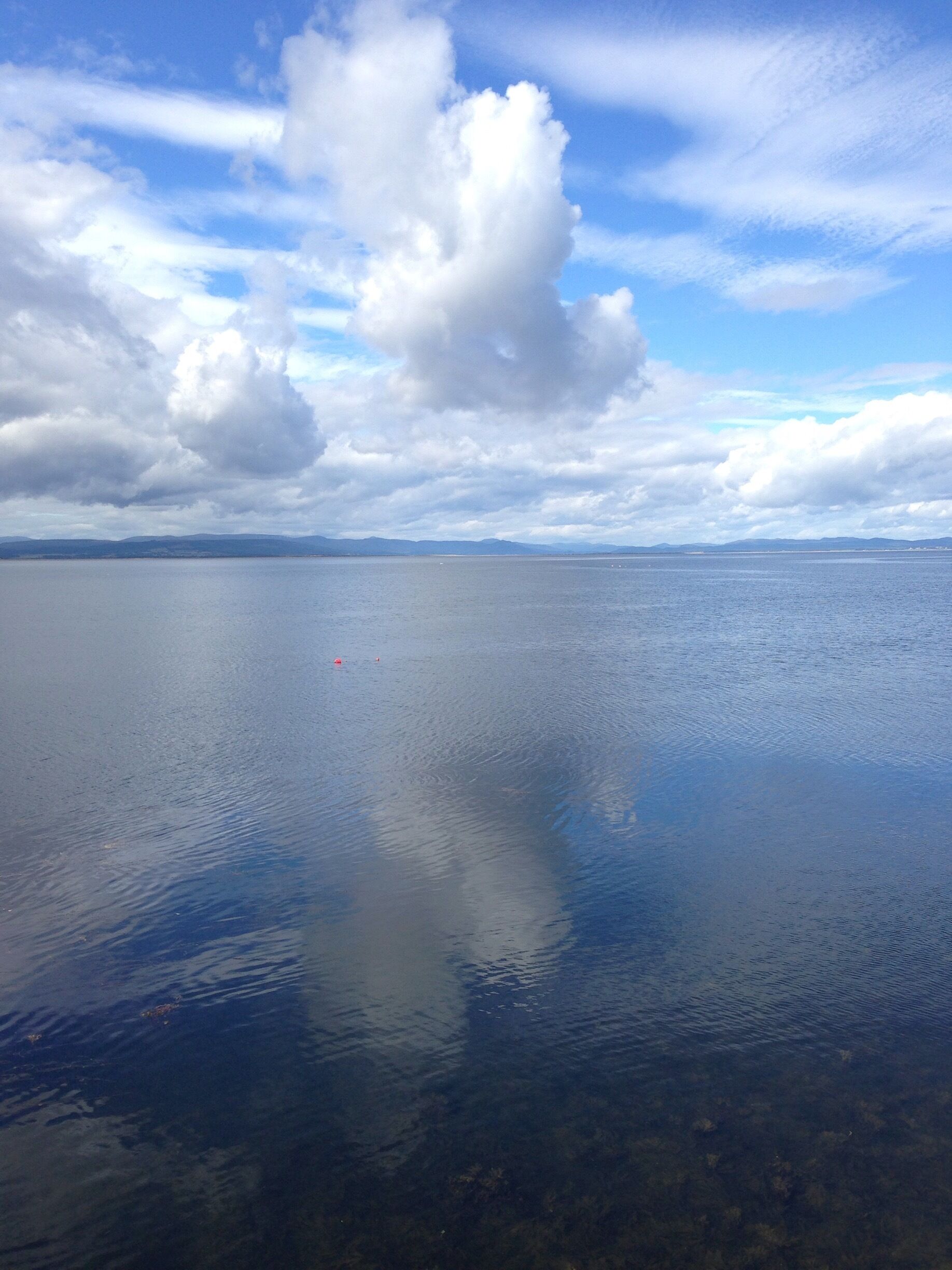 A calm body of water with a clear sky and distant mountains.