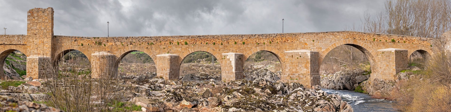 A stone bridge with multiple arches over a rocky riverbed.