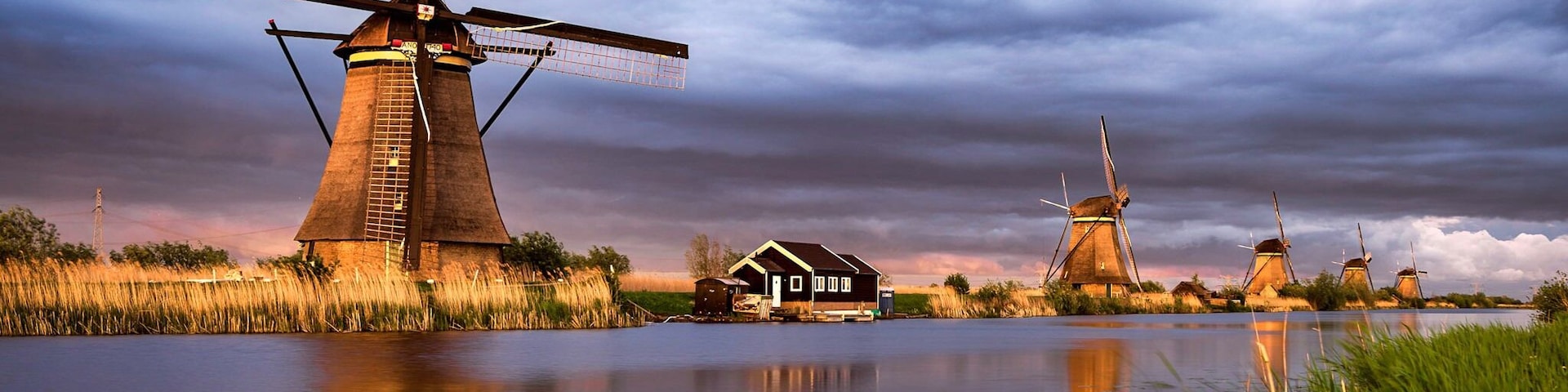 Kinderdijk is located a short drive from Rotterdam. Very beautiful and iconic location with 19 gorgeous classic windmills placed perfectly along the canal, giving some great reflections in your photos.
Not many parking spots, so during the day, it can be hard to find a spot. This is no problem when the attraction is closed, so a great spot for sunrise/sunset shoots.
Here is a photo of some of the mills during sunset. The sky was very dark, but the sun peaked through the clouds and lit up the mills, creating a unique and gorgeous scene.