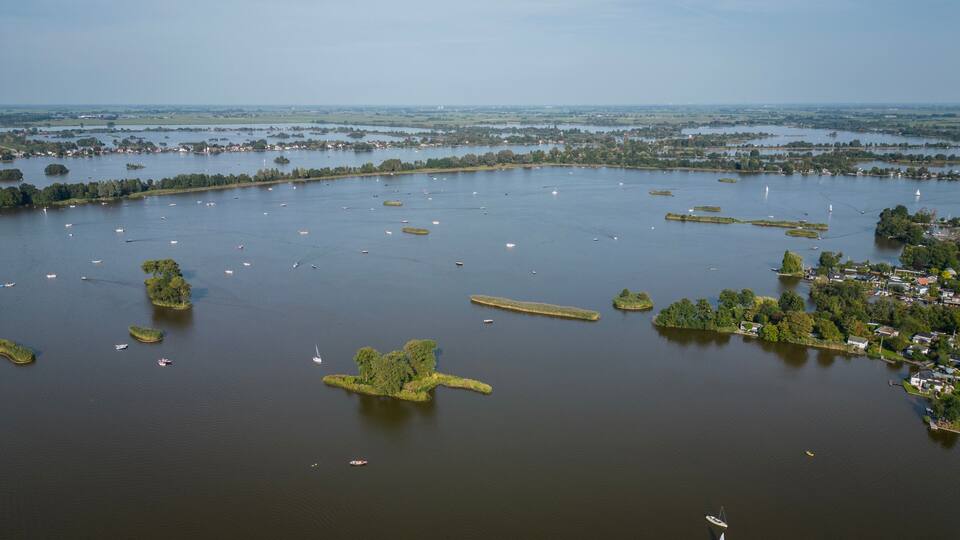 An aerial view of a large lake with numerous boats, surrounded by greenery and small islands.