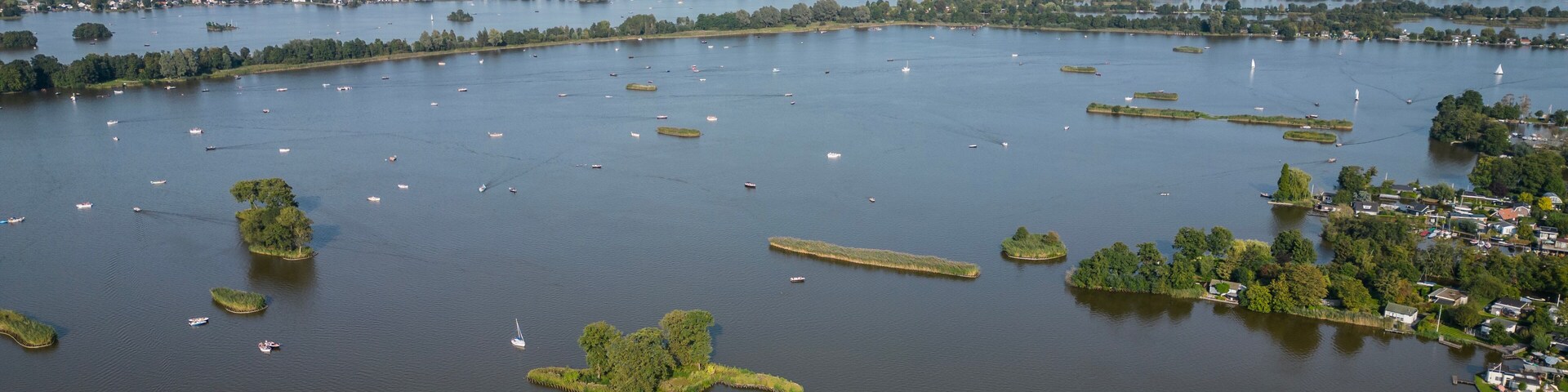 Vista aérea de um lago grande com muitos barcos, rodeado por vegetação e pequenas ilhas.