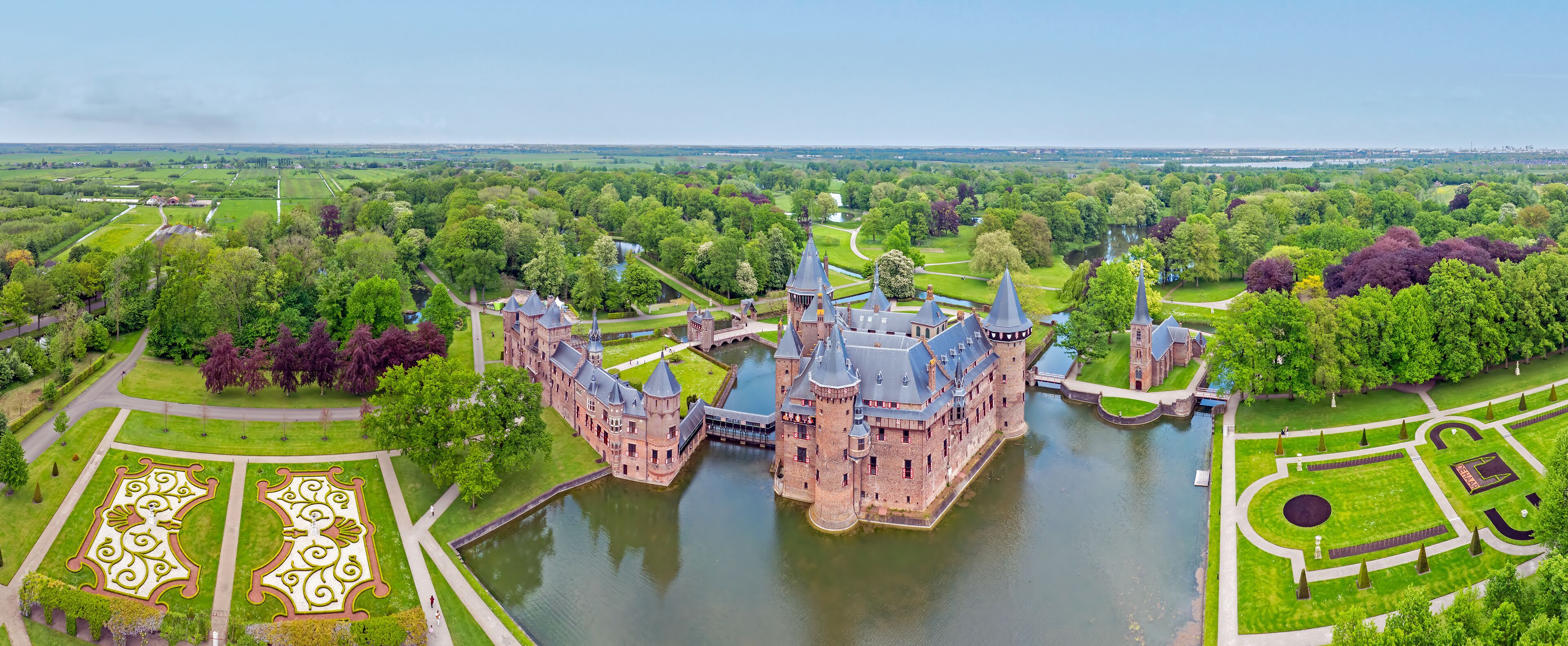 A castle surrounded by a moat, lush greenery, and a river.
