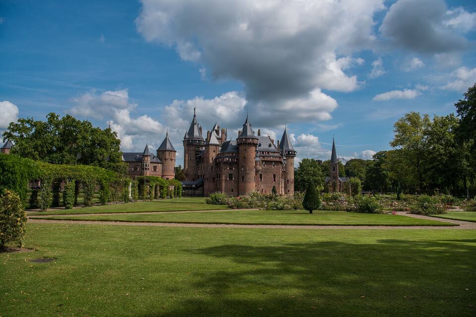 A large castle with multiple towers and turrets, surrounded by well-maintained gardens and trees.