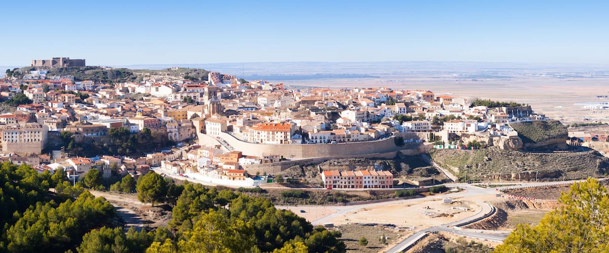 A historic town with a prominent castle on a hill, surrounded by dense greenery and a clear sky.