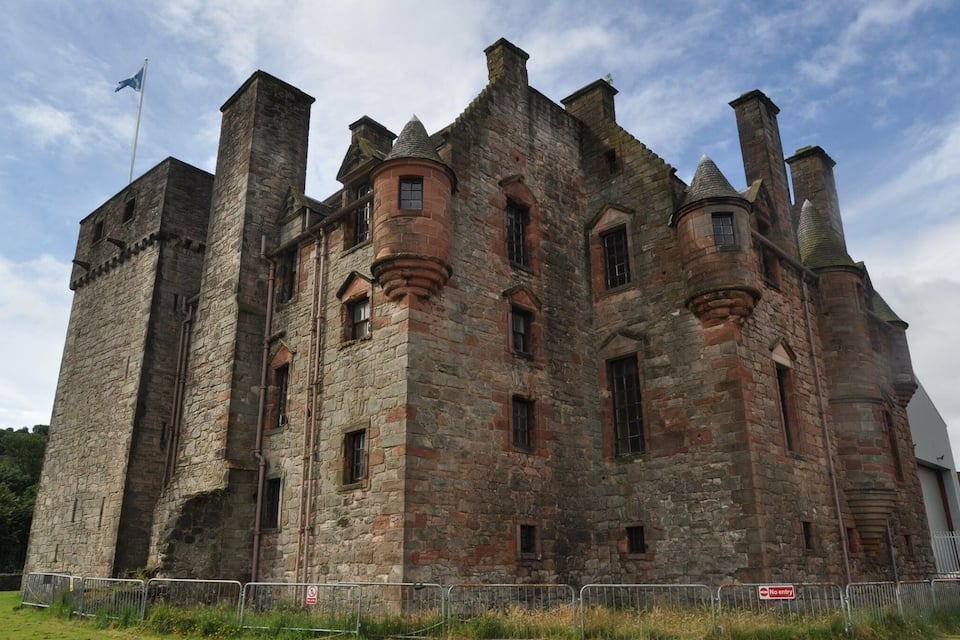 Un grand château en pierre, doté de nombreuses tours et surmonté d’un drapeau.