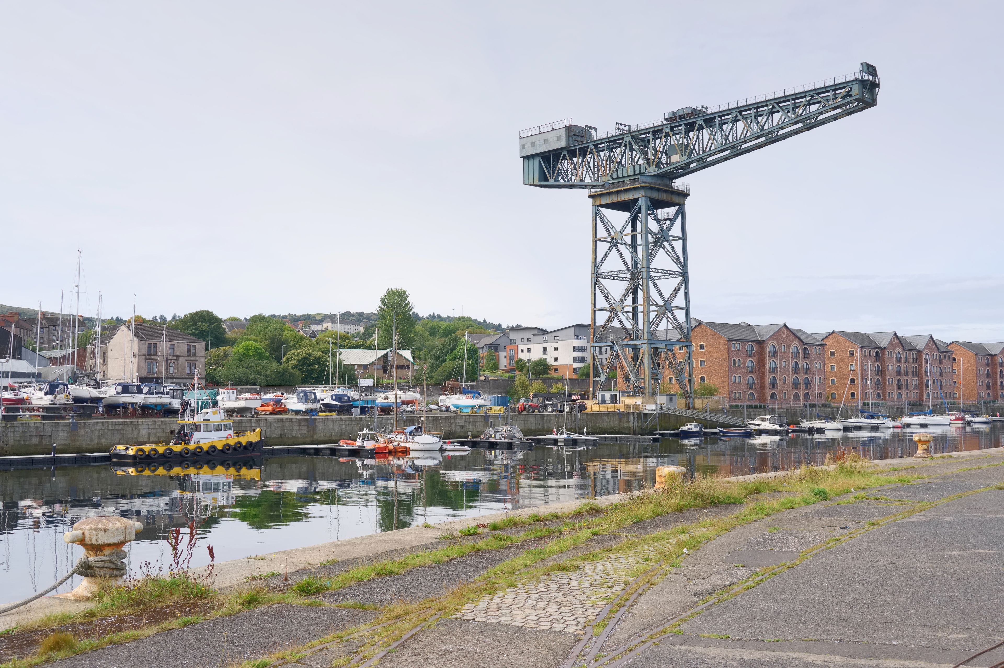 A harbor with boats, a large crane, and buildings in the background.
