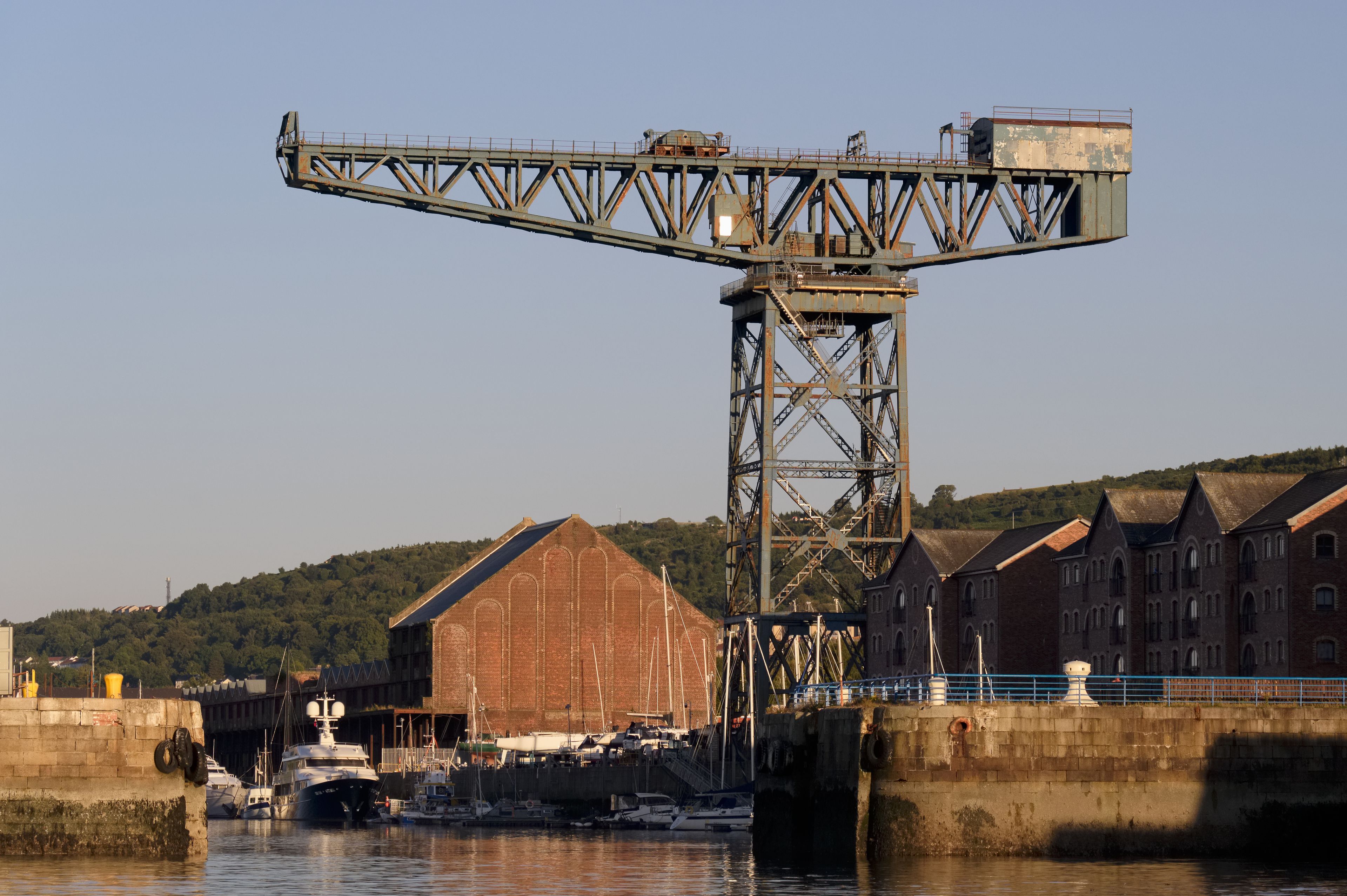 A large industrial crane, a historic brick building, and a harbor with boats.
