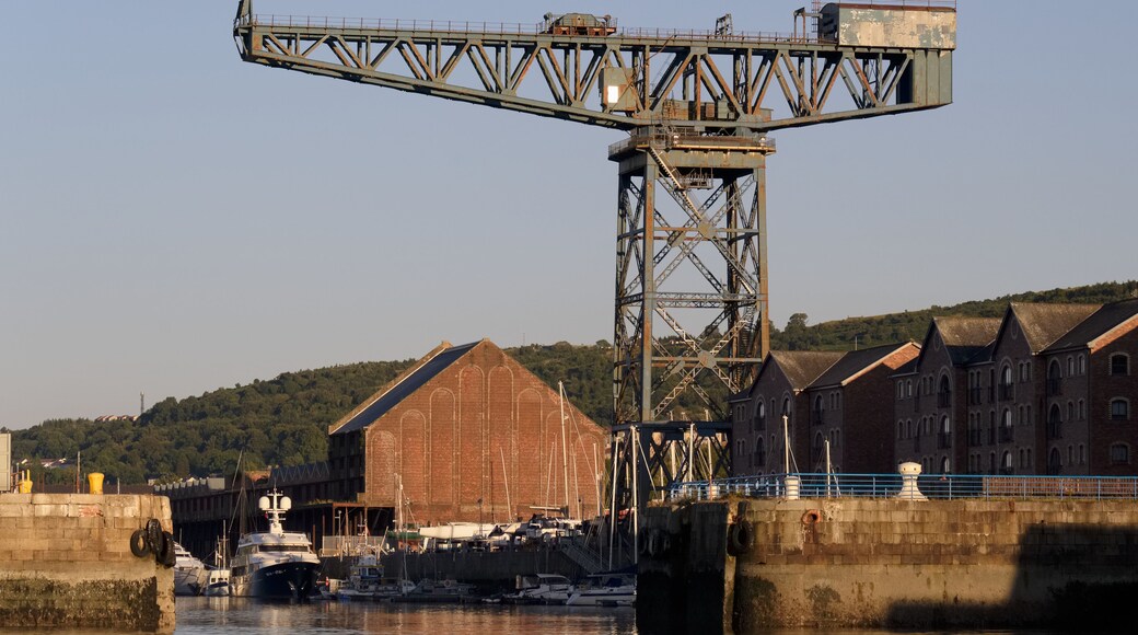 A large industrial crane, a historic brick building, and a harbor with boats.