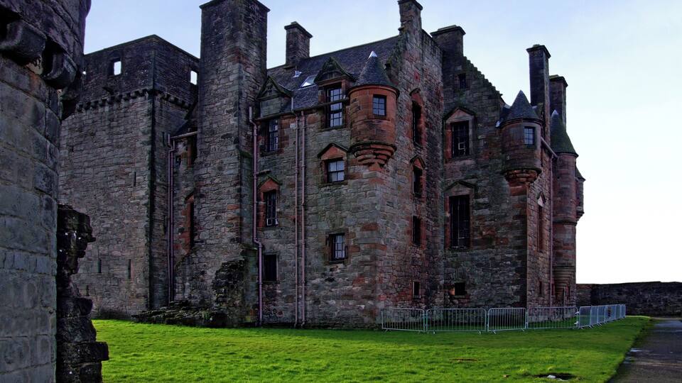 A historic stone castle with multiple towers and turrets, surrounded by a well-maintained lawn.