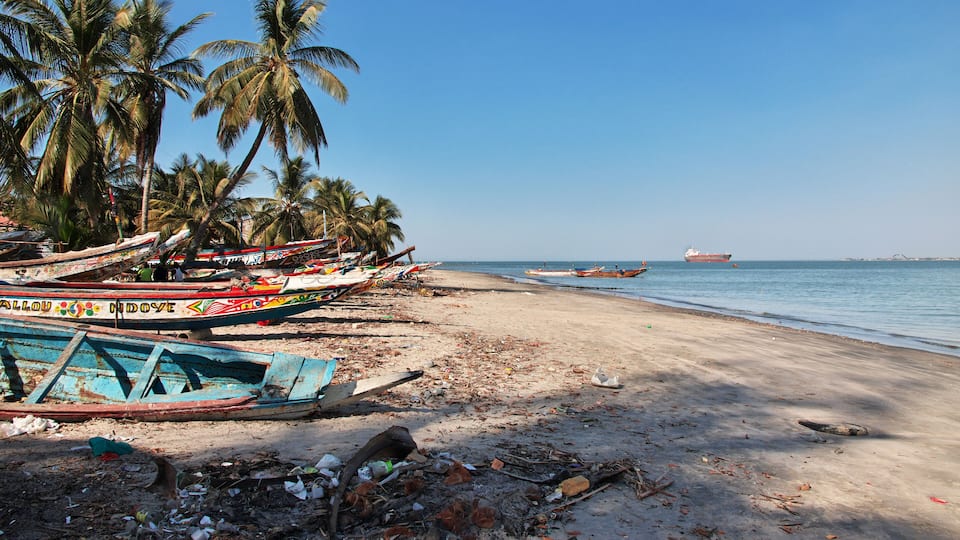 A beach with palm trees, boats, and a ship in the water.