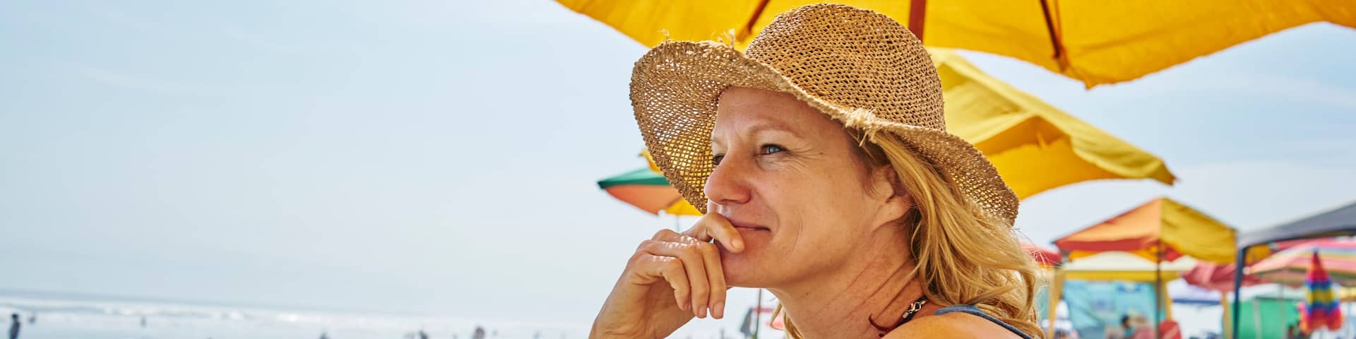 A beach scene with a person under a yellow umbrella, sandy beach, and ocean in the background.