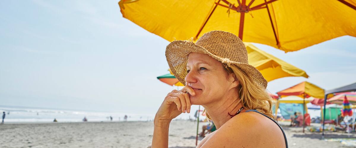 A beach scene with a person under a yellow umbrella, sandy beach, and ocean in the background.