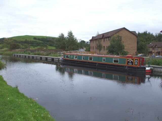 A narrowboat on a calm river, surrounded by greenery and a brick building.