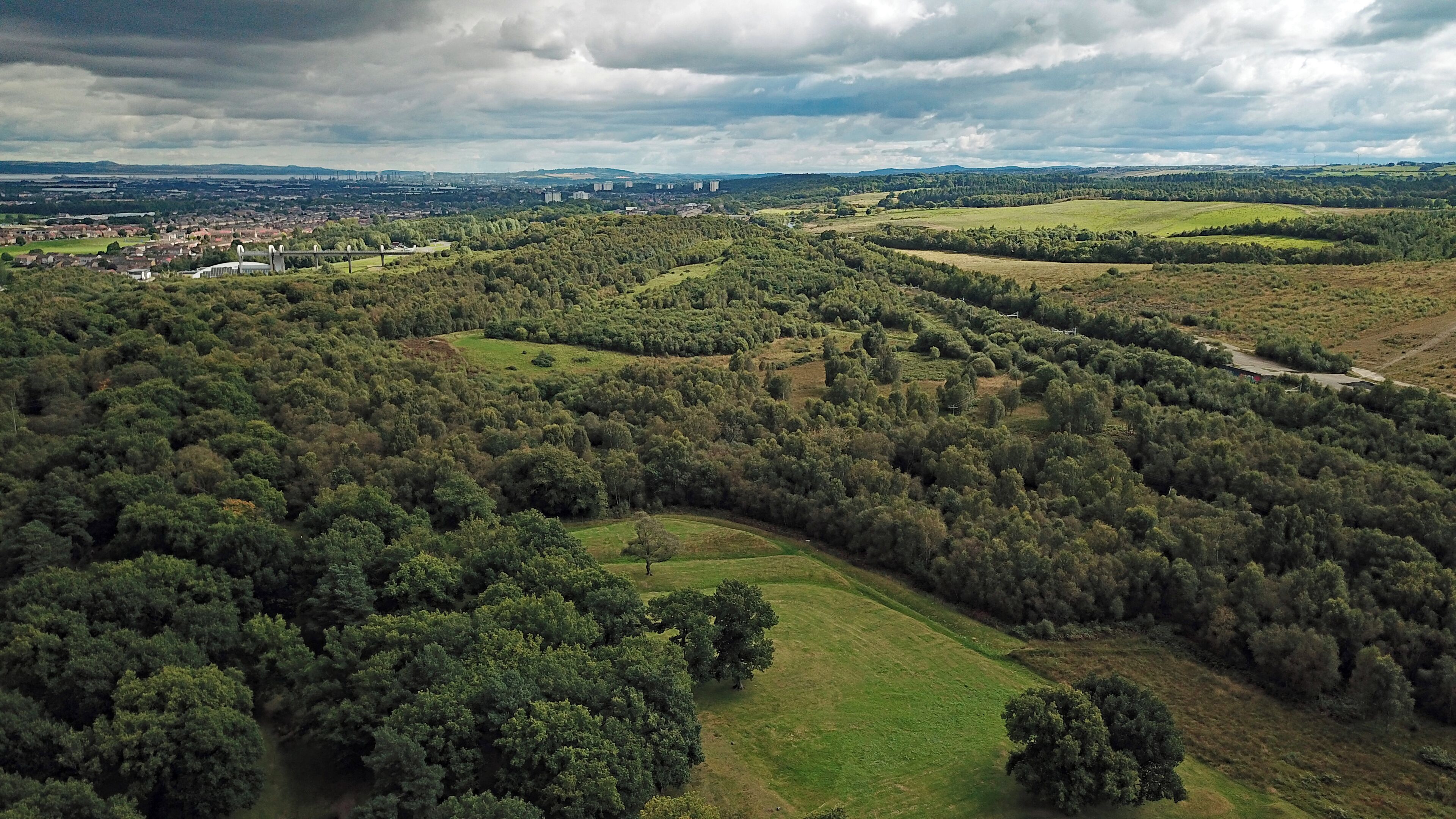 An aerial view of a densely forested area with rolling hills and a distant urban skyline.