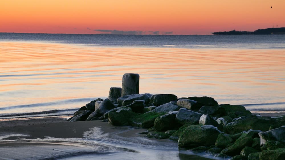 A rocky shoreline with a sunset over the water.