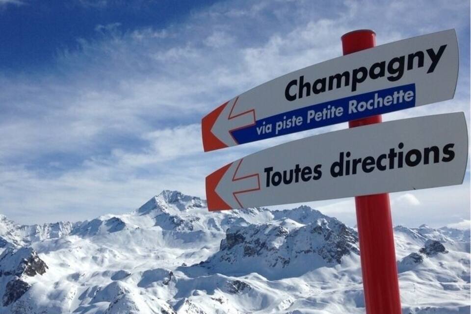 A signpost with directions to Champagny and Petite Rochette, and a mountain range in the background.