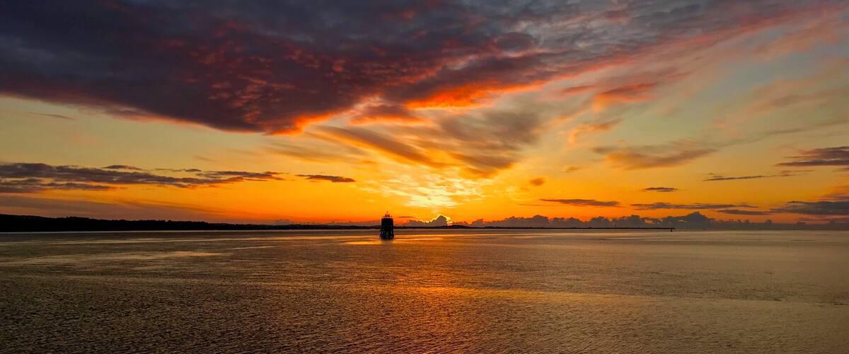 A sunset over a calm body of water with a distant shoreline silhouette.