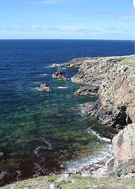 Um litoral rochoso com águas azul-claras e vista para o oceano.