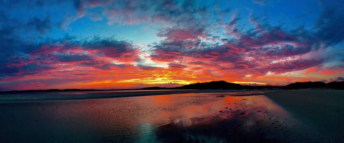 A beach at sunset with vibrant red and orange clouds reflecting on the wet sand.