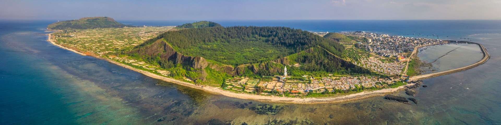 An aerial view of a coastal town with a prominent lighthouse, a densely populated area, and a clear blue sea.