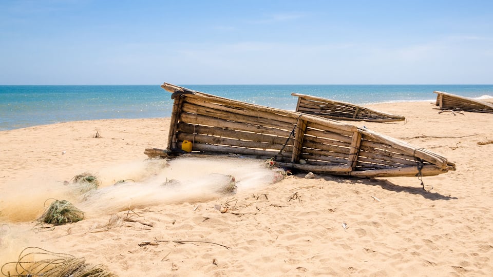 A sandy beach with several wooden boats and some seaweed scattered around.