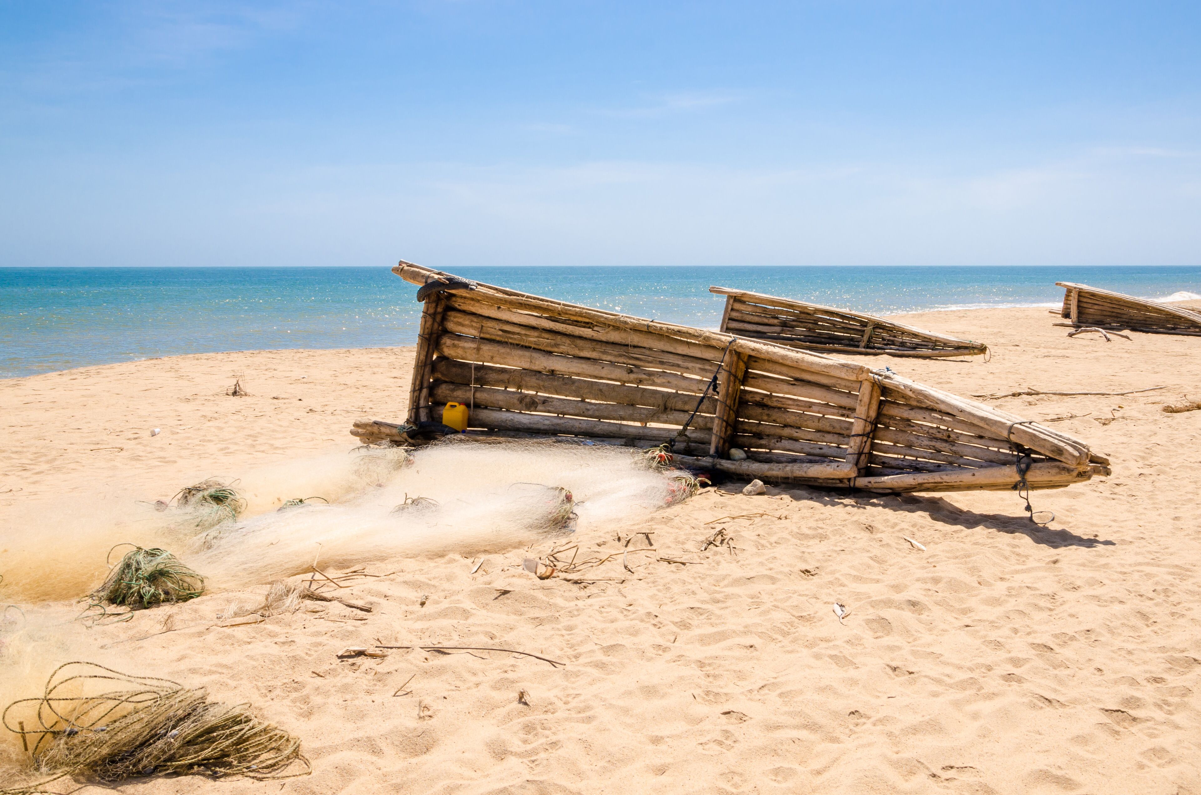 A sandy beach with several wooden boats and some seaweed scattered around.