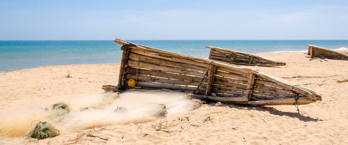 A sandy beach with several wooden boats and some seaweed scattered around.