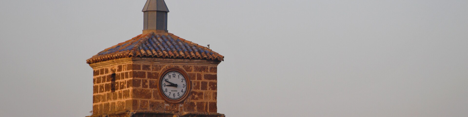 Una torre de reloj de ladrillo con un veleta en la parte superior.