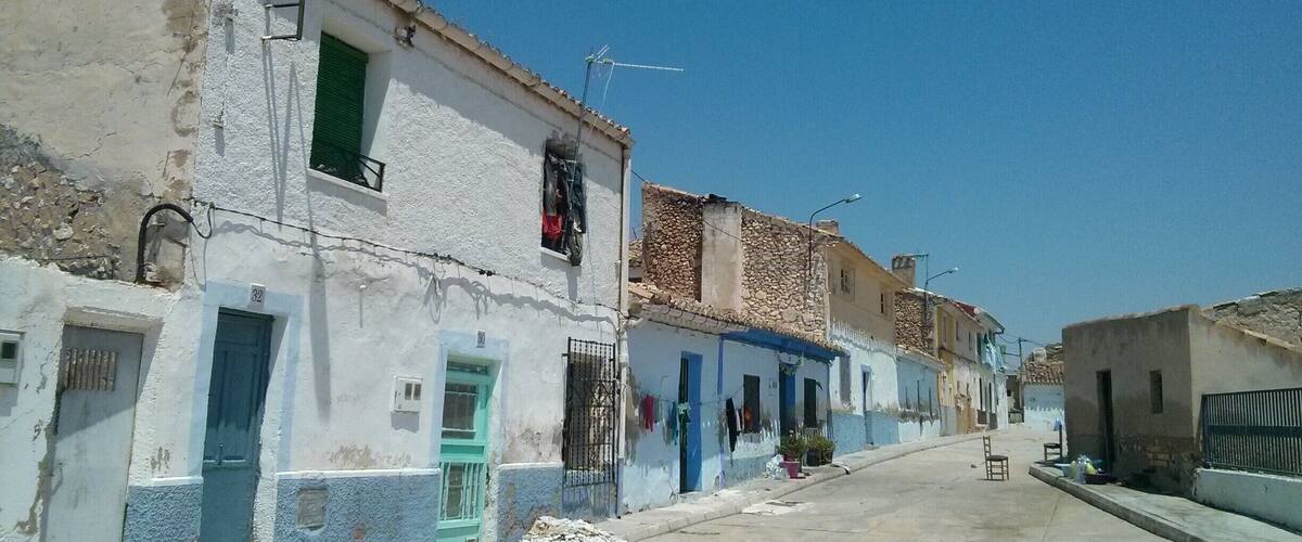 A quiet street with old buildings, some with blue trim, and a clear blue sky.