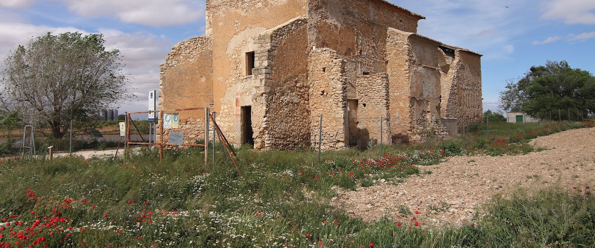 An old stone building with a tower, surrounded by wildflowers and a clear sky.