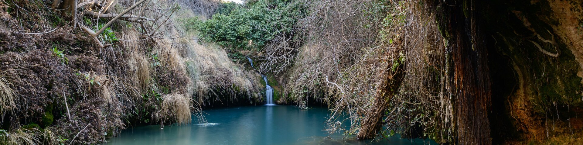 Une rivière paisible avec une cascade, entourée d’une végétation luxuriante et d’un paysage rocheux.